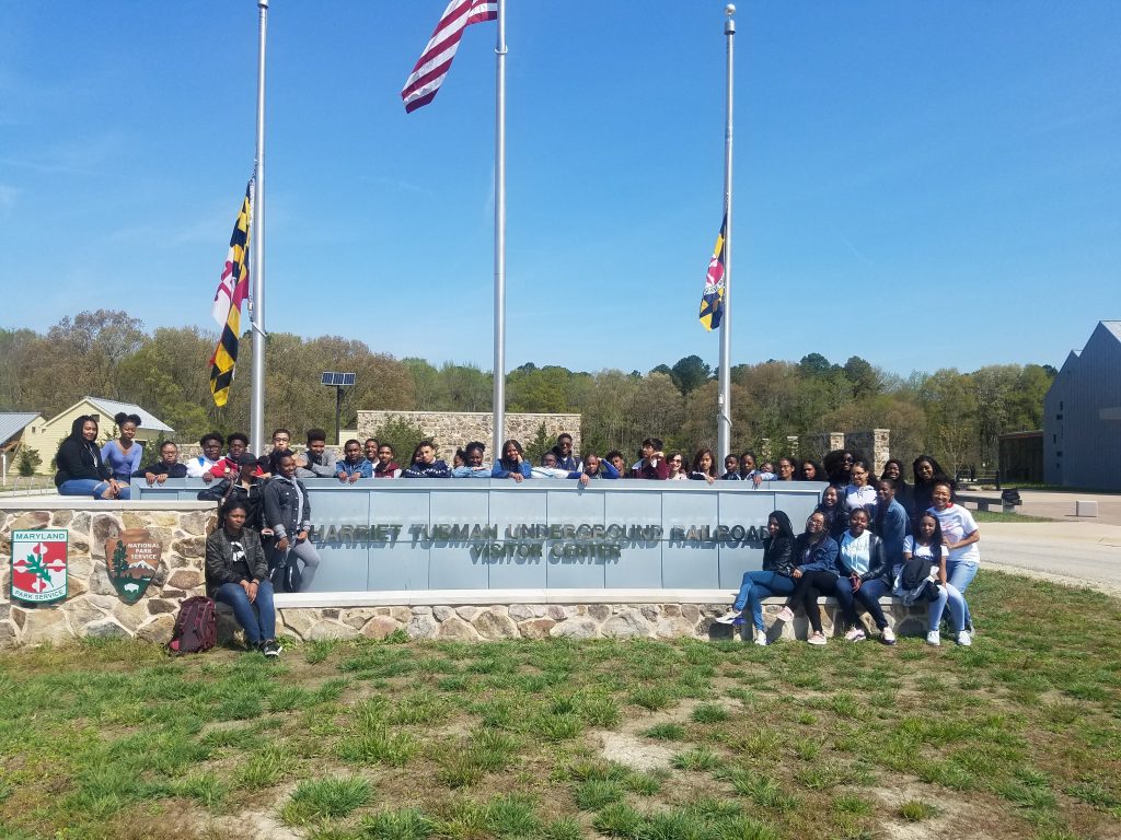 students posing near the visitor center sign